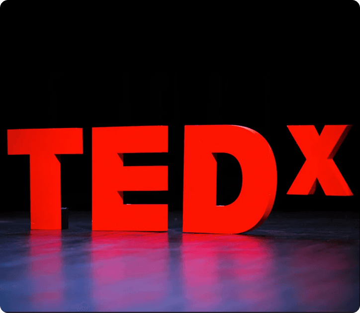 Large red TEDx letters on a stage with a dark black background and purple light reflection on the floor