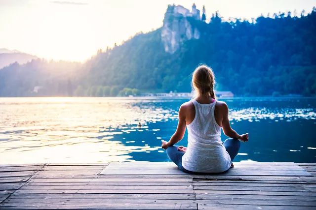 A woman sitting on the dock of a lake meditating.